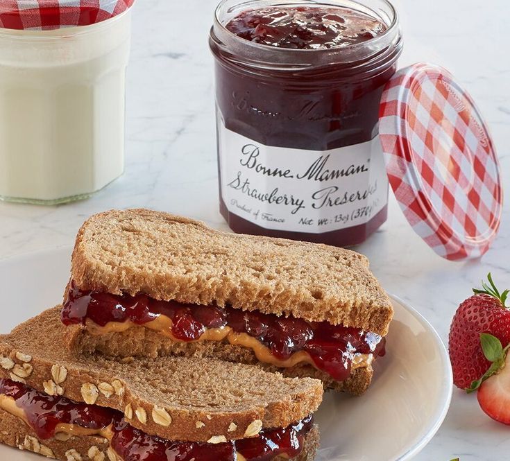 two peanut butter and jelly sandwiches on a plate with strawberries next to the jar