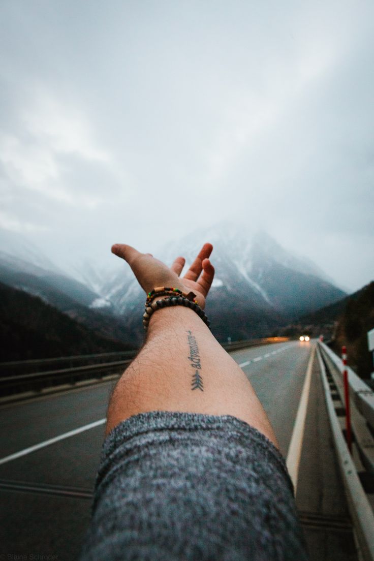 a person holding their hand out on the side of a road with mountains in the background