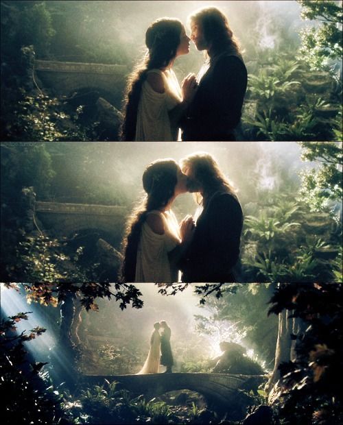 two people standing next to each other in front of trees and bushes, one is kissing the other's forehead