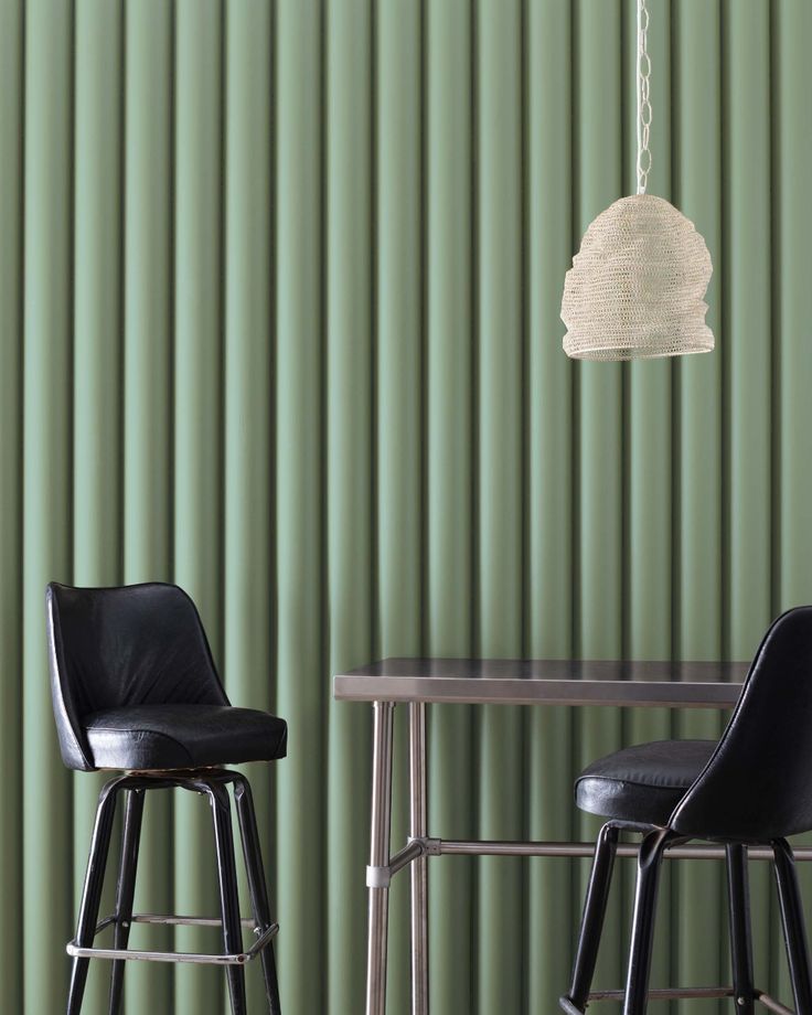 two chairs and a table in front of a green wall with vertical blindes on it