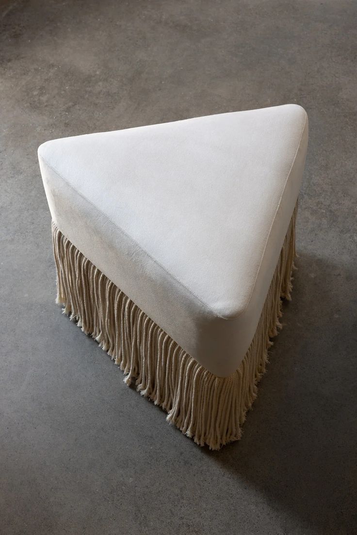 an upholstered white bench with fringes on the bottom and back end, sitting on concrete flooring