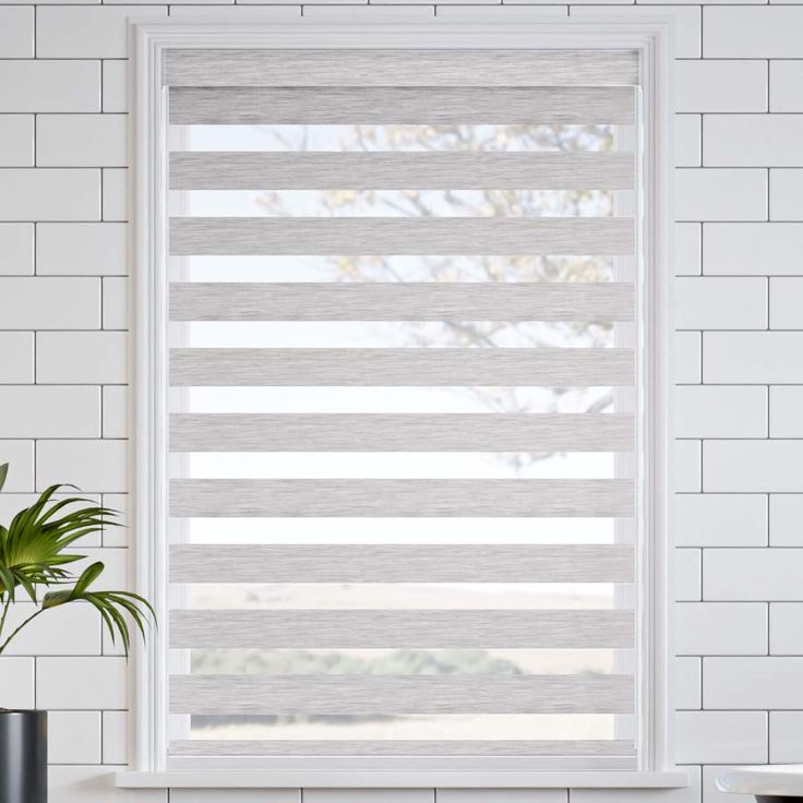 a white brick wall with a window covered in blinds and a potted plant next to it