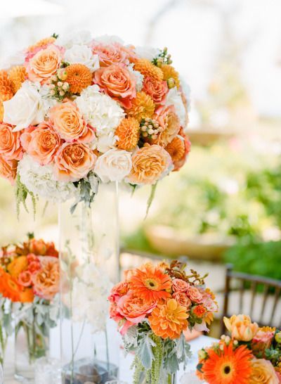 an arrangement of orange and white flowers in vases on a table with other decorations