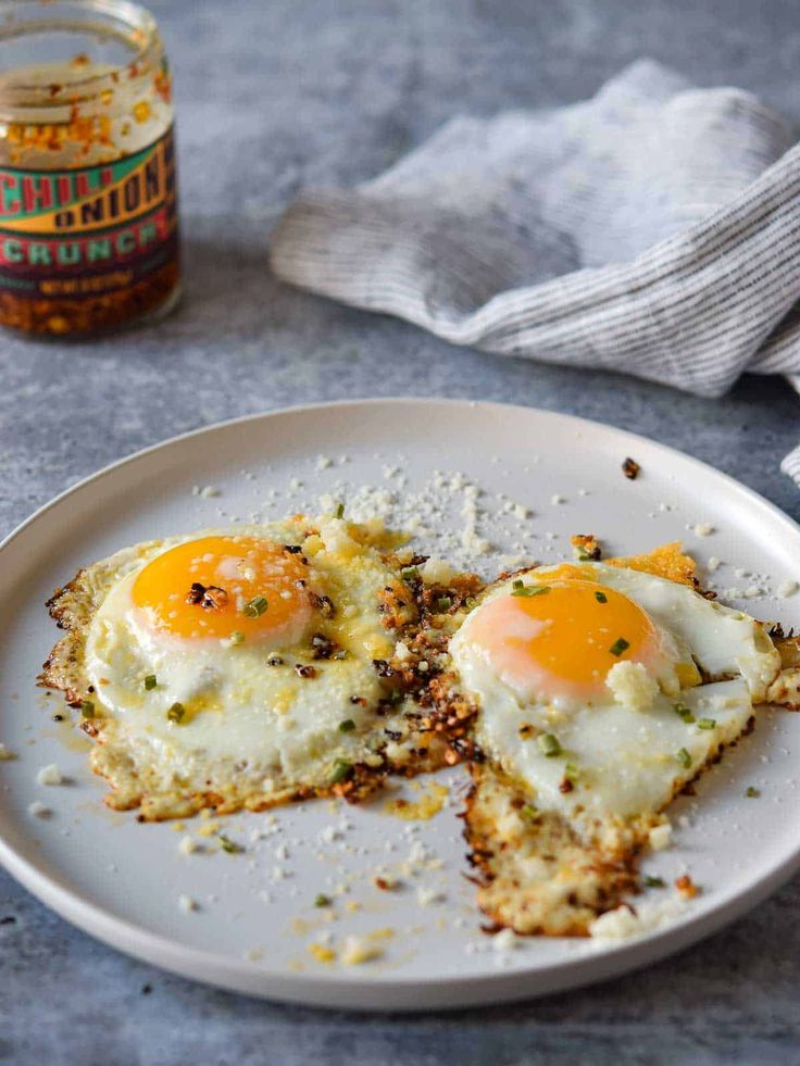 two fried eggs sitting on top of a white plate next to a jar of mustard