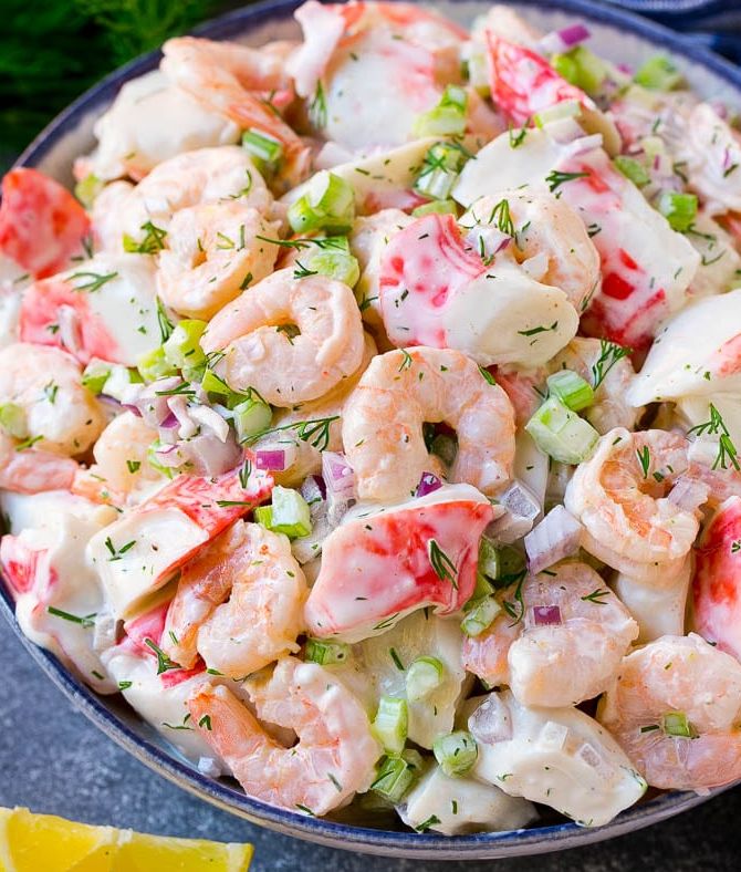 a bowl filled with shrimp salad next to lemon wedges