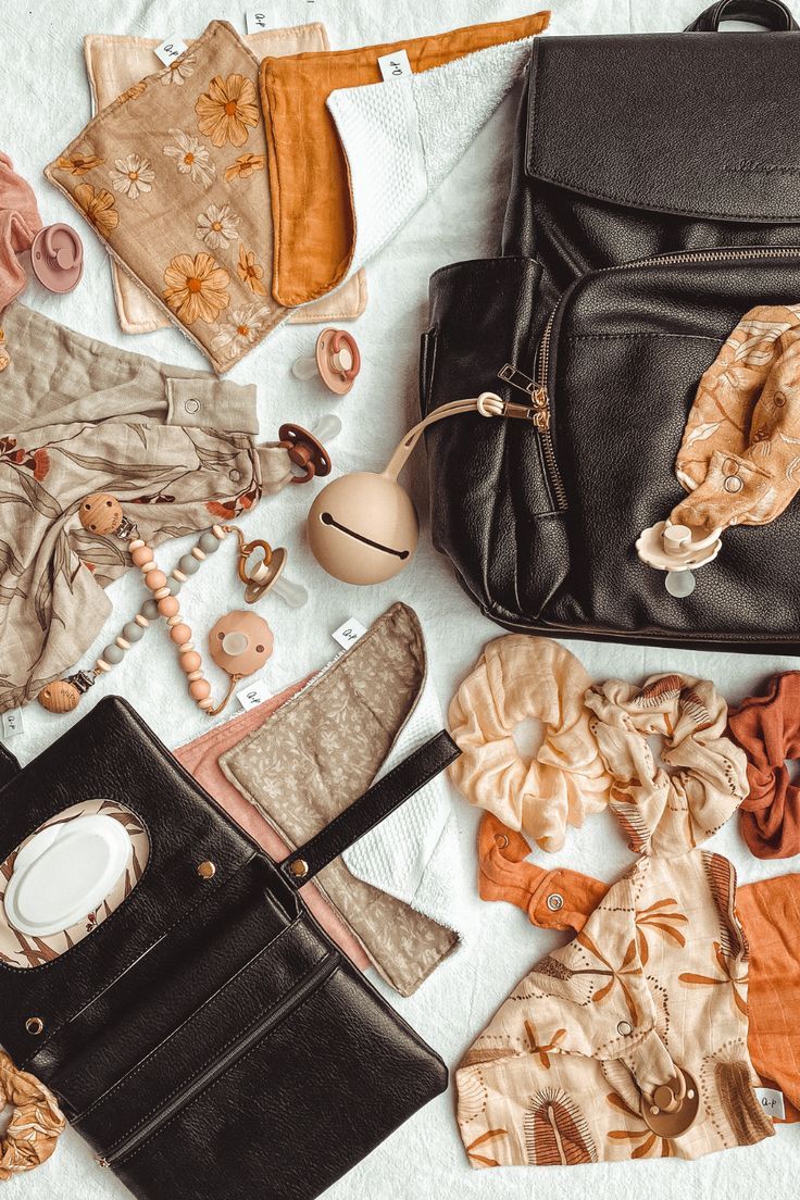 an assortment of clothing and accessories laid out on a bed next to a purse, cell phone