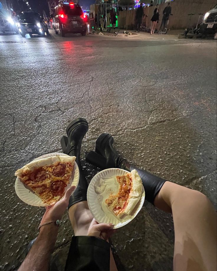 two people holding plates with slices of pizza on them in the middle of the street