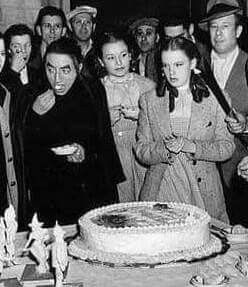 a group of people standing around a table with a cake in front of them on it