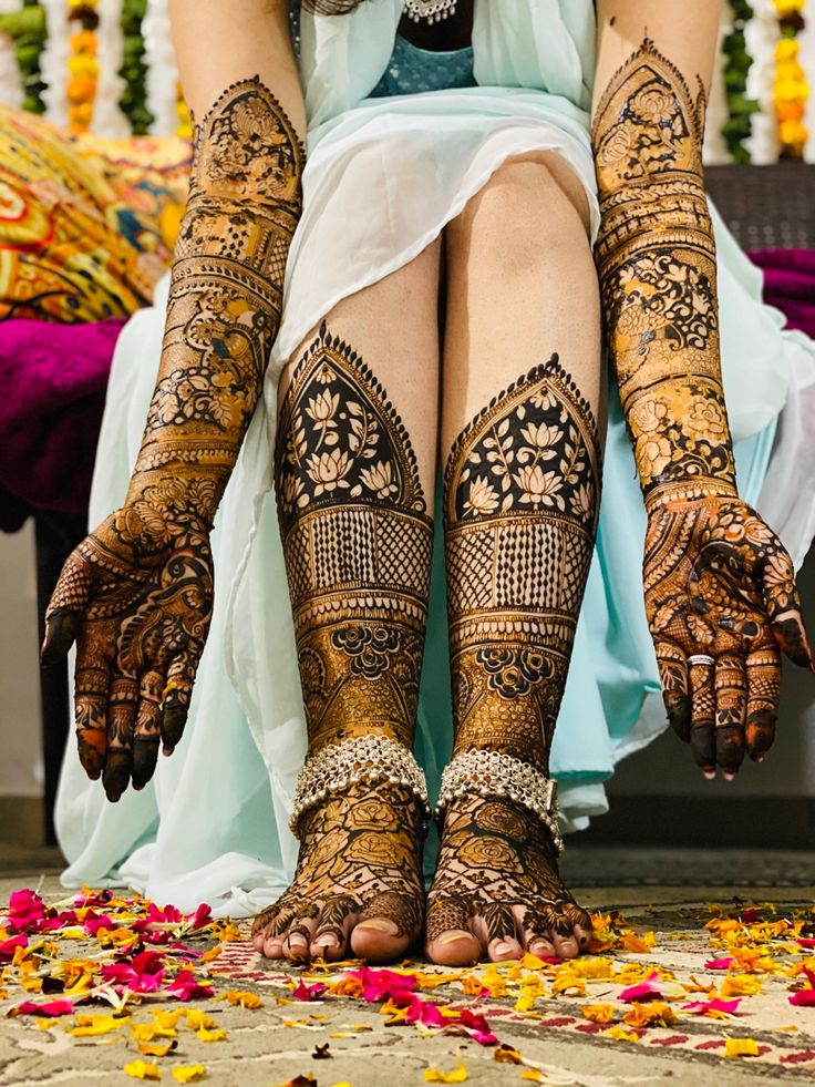 the legs and feet of a woman with henna tattoos on their hands, sitting in front of flowers