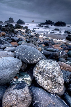 many rocks on the beach with water in the background and dark clouds overhead above them