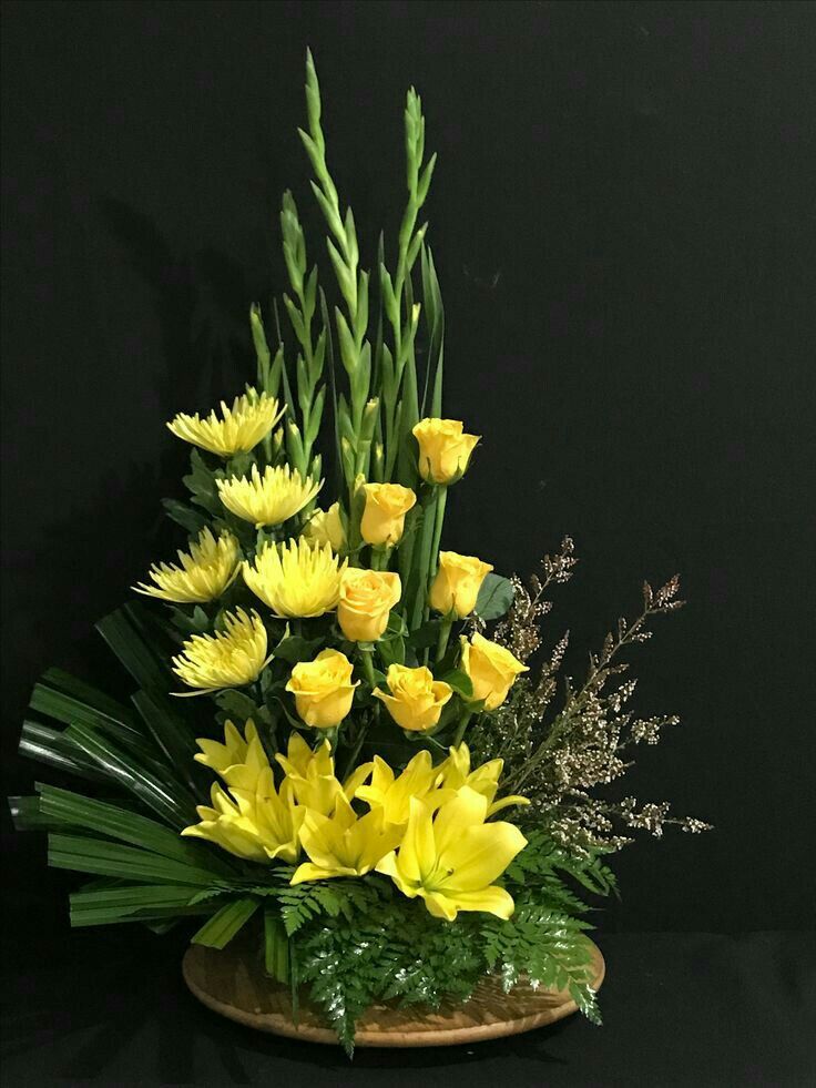 a basket filled with yellow flowers sitting on top of a black table next to greenery