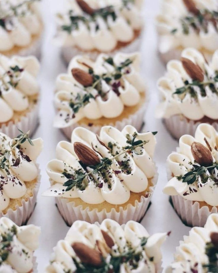 many cupcakes with white frosting and toppings on them are arranged in rows