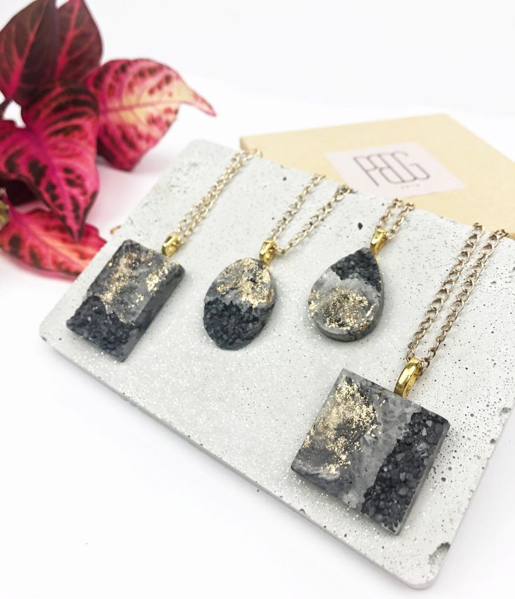 three necklaces with black and white designs on them sitting next to a plant in a box