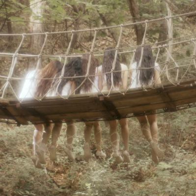 four women are walking across a rope bridge in the woods with long hair on them