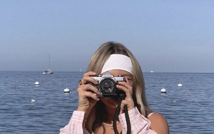 a woman taking a photo with her camera near the ocean and boats in the water