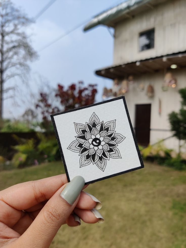 a person holding up a small card with a flower on it in front of a house