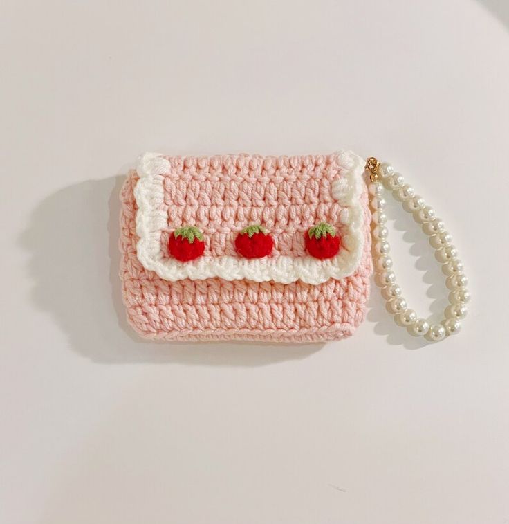 a pink crocheted purse with two strawberries on the front and white trim