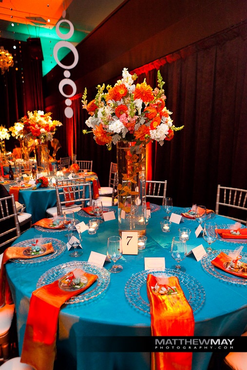 a blue table topped with plates and vases filled with orange and white flowers on top of it