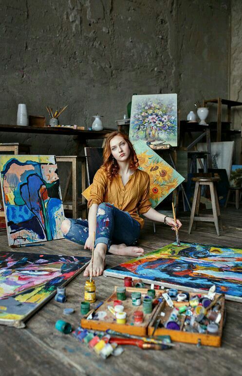 a woman is sitting on the floor in front of her art work and paintbrushes