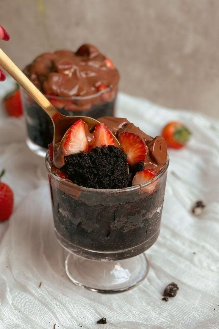 two desserts with chocolate pudding and strawberries in them on a white tablecloth