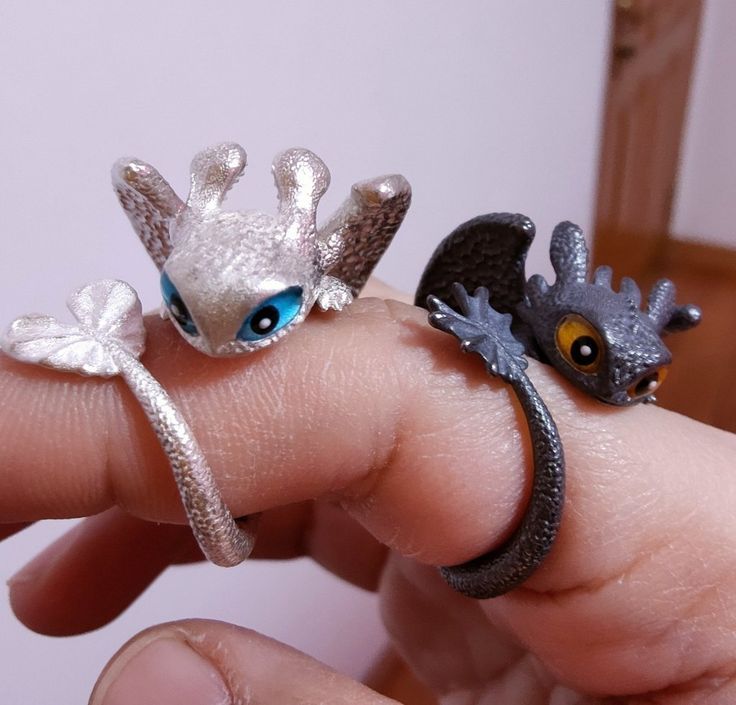 two tiny rings are sitting on someone's finger, one has a dragon and the other is a bird