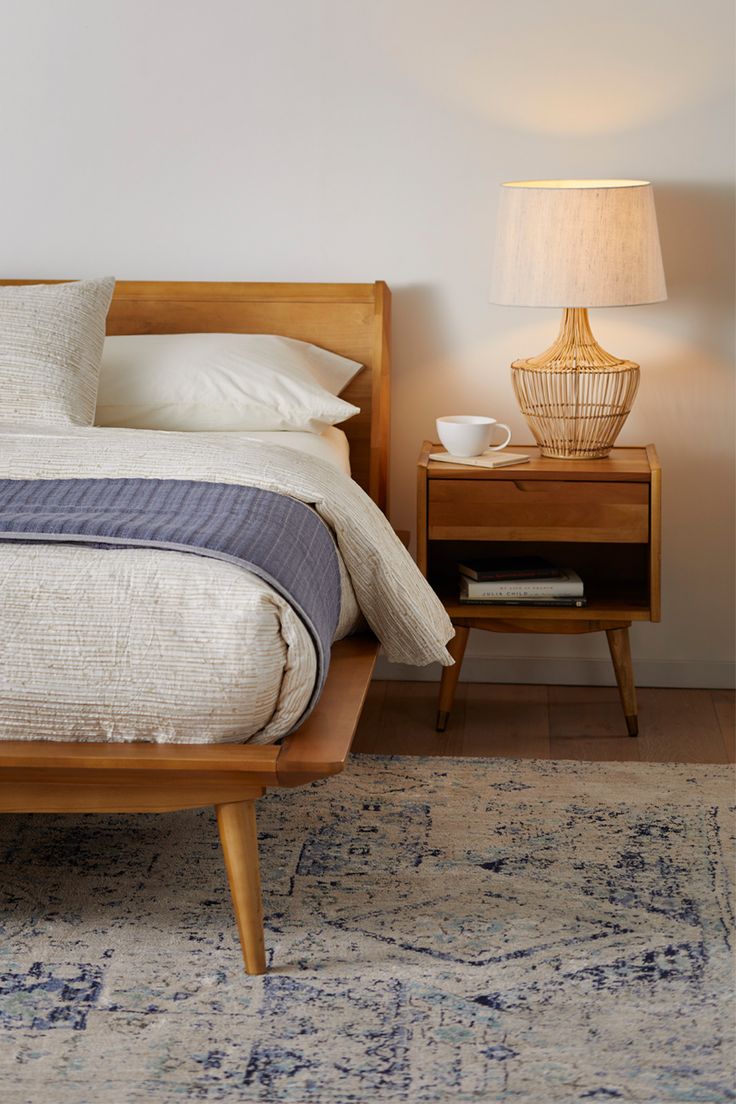 a bed sitting next to a night stand with a lamp on top of it in a bedroom