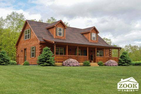 a large log cabin home in the middle of a grassy field with trees and bushes