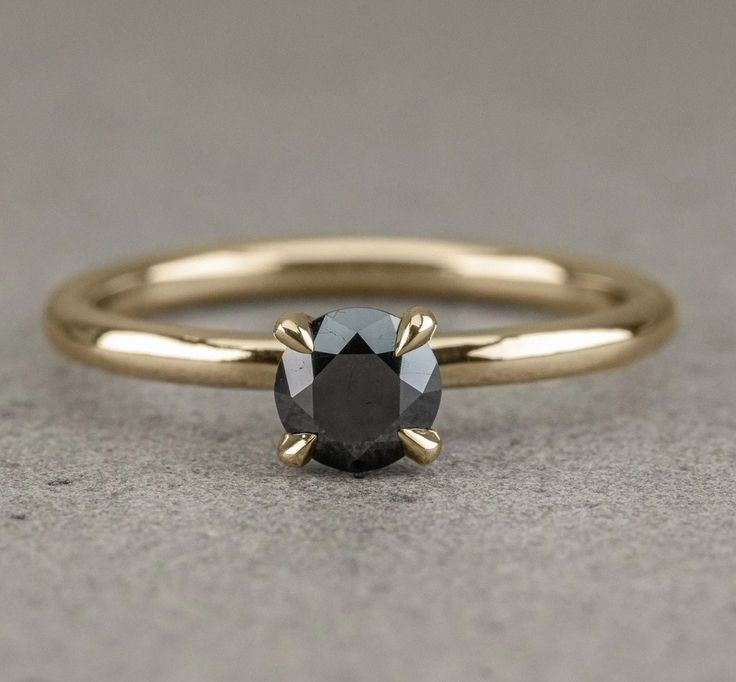 a black diamond ring sitting on top of a gray surface with the center stone in rose gold