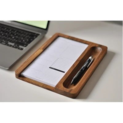 a desk with a laptop, pen and paper on it next to a wooden tray