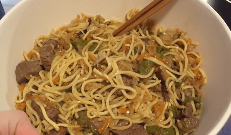 someone holding chopsticks over a bowl of noodles with meat and vegetables in it