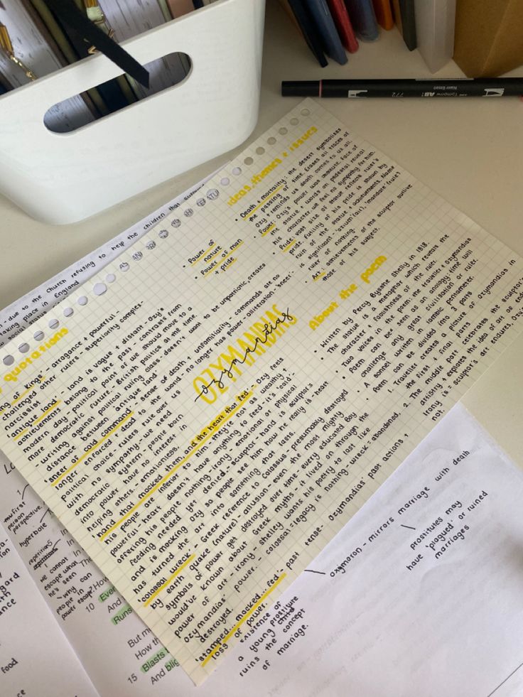 two pieces of paper with yellow writing on them next to a pen and some pens