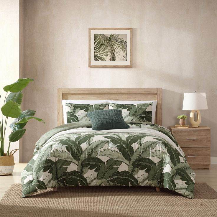 a bed in a room with a green comforter and pillows on the floor next to a potted plant