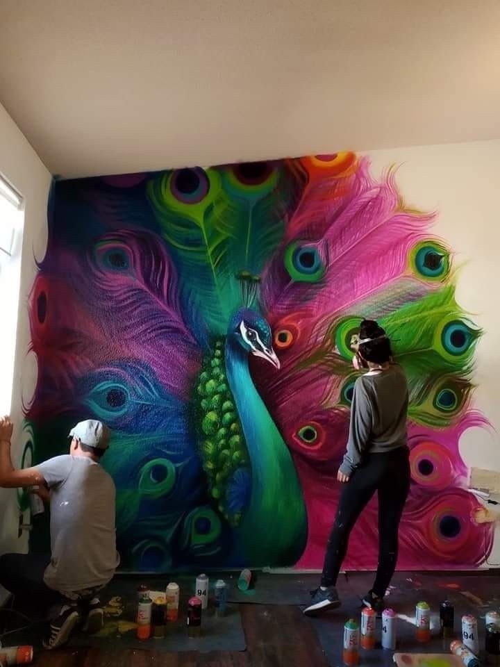 two men are painting a peacock mural on the wall