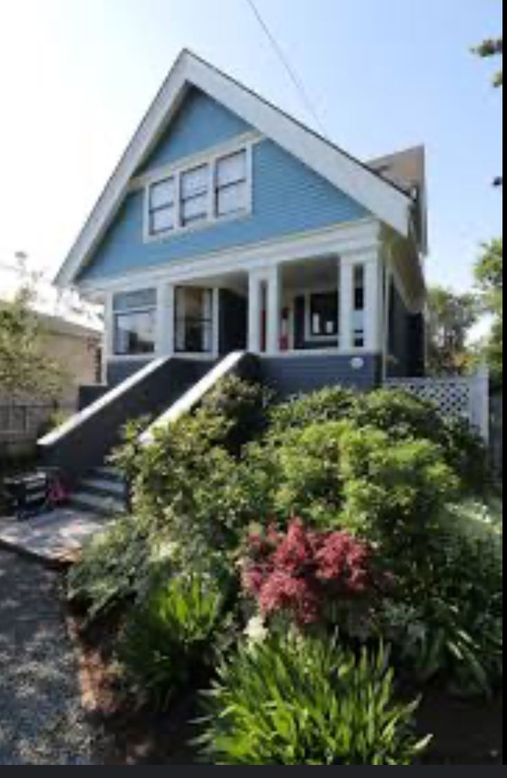 a blue house sitting next to a lush green tree and shrub covered yard with steps leading up to the front door