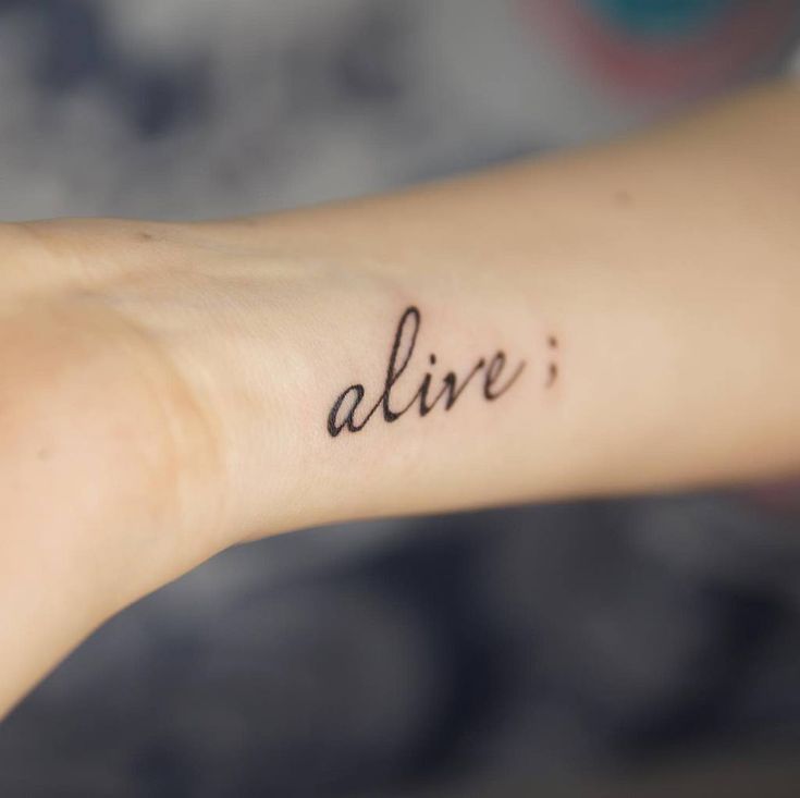 the word alive is written in cursive ink on a woman's arm