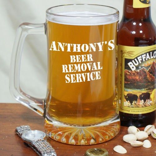 a beer glass next to a bottle and some peanuts on a table with a spoon