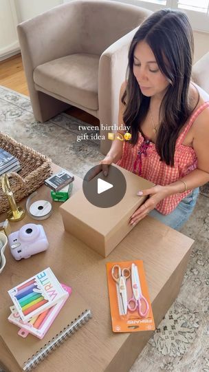 a woman opening a box with scissors and other items on the table in front of her