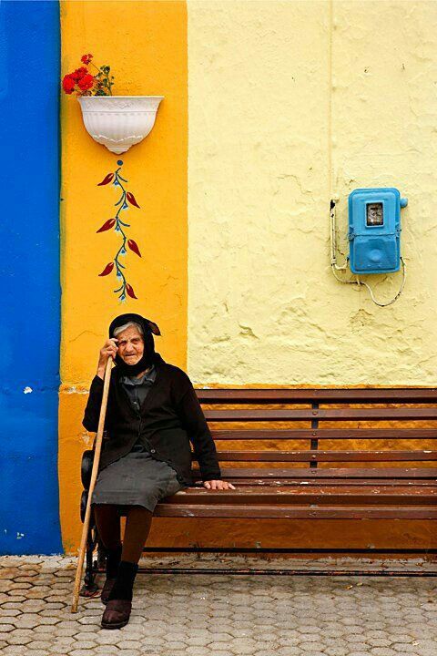 a woman sitting on a bench in front of a yellow and blue wall holding a stick