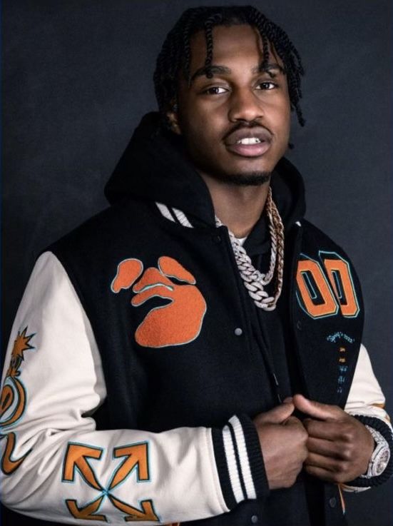 a man with dreadlocks wearing a black jacket and orange lettering on the sleeves