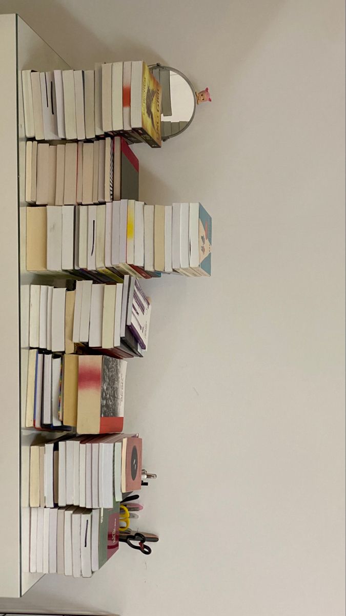 a book shelf filled with lots of books next to a wall mounted mirror on the side of a white wall