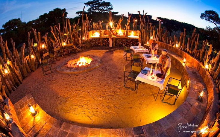 a fire pit surrounded by chairs and tables with lit candles on the table in front of it