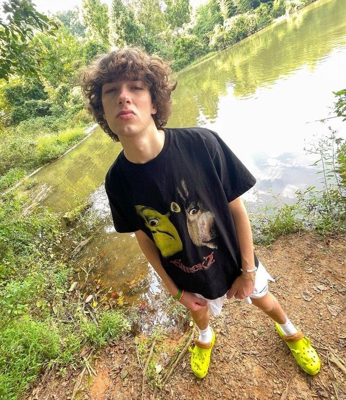 a young man standing next to a body of water wearing yellow shoes and a black t - shirt