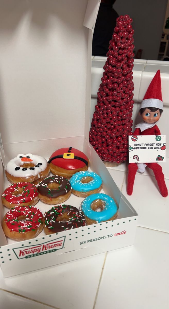 an elf is sitting next to a box of doughnuts