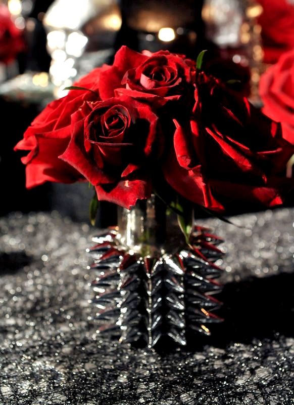 some red roses in a vase on a table with silver sparkles and candles behind them