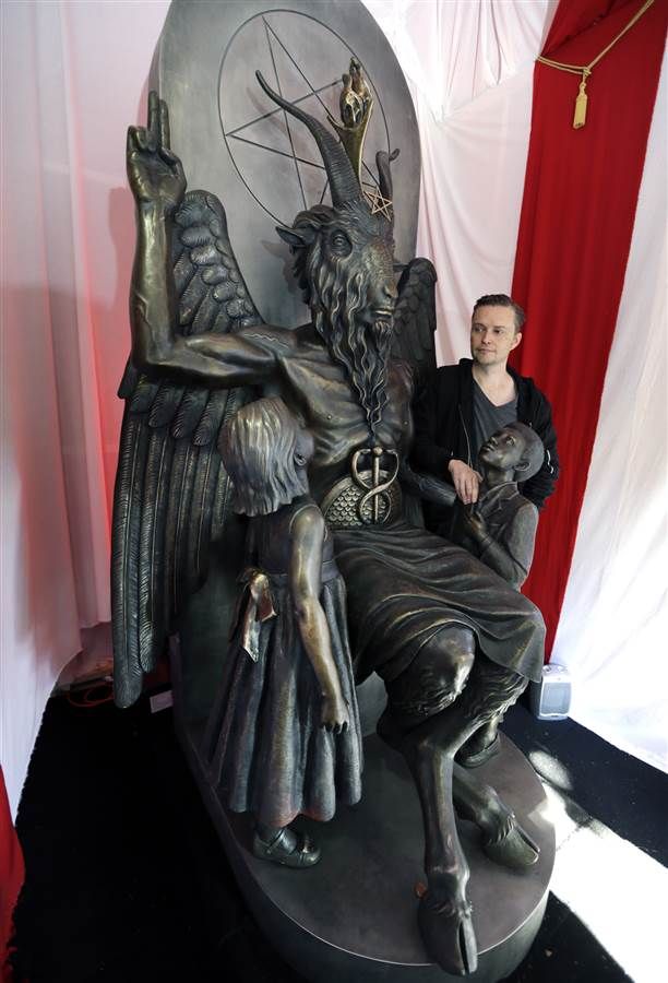 a man sitting on top of a statue in front of a red curtain