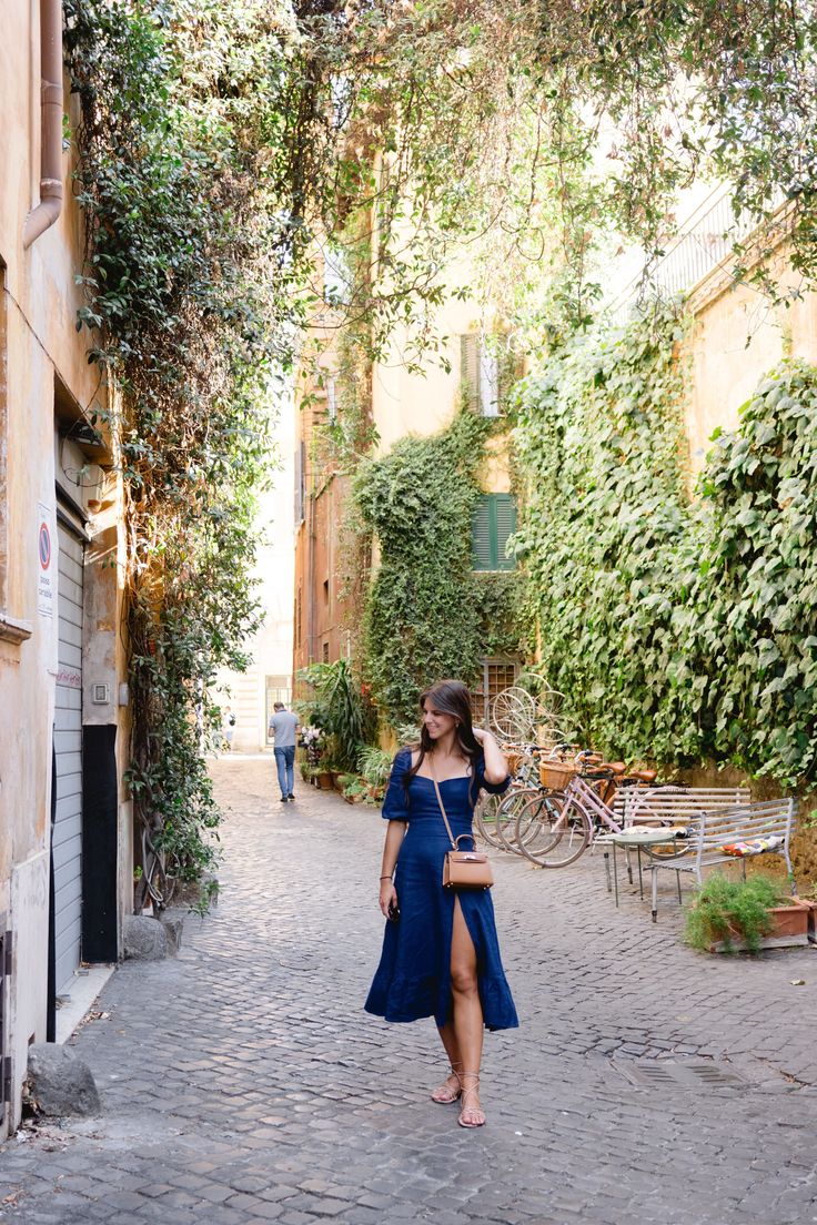 a woman in a blue dress is walking down an alley way with trees on either side