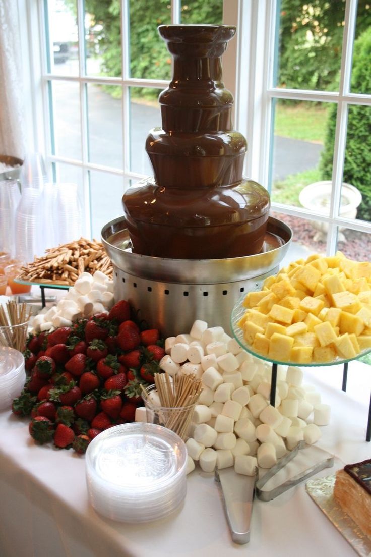 chocolate fountain with marshmallows, strawberries and other desserts on the table