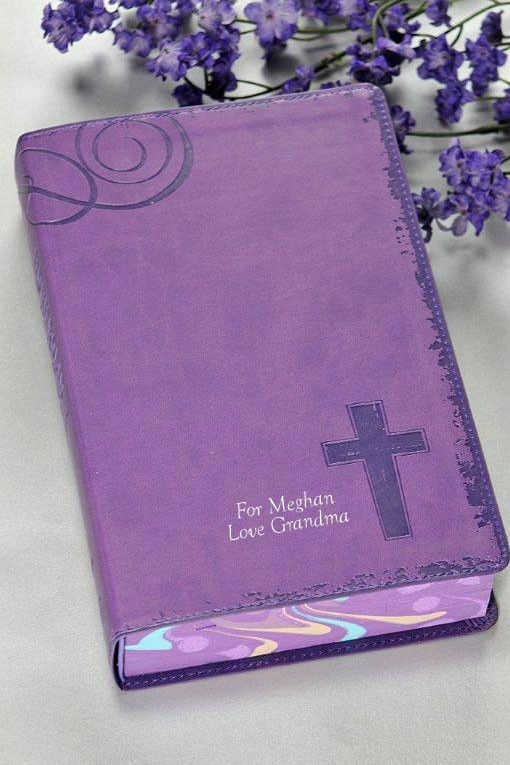 a purple book with a cross on it next to some lavender flowers and a glass vase