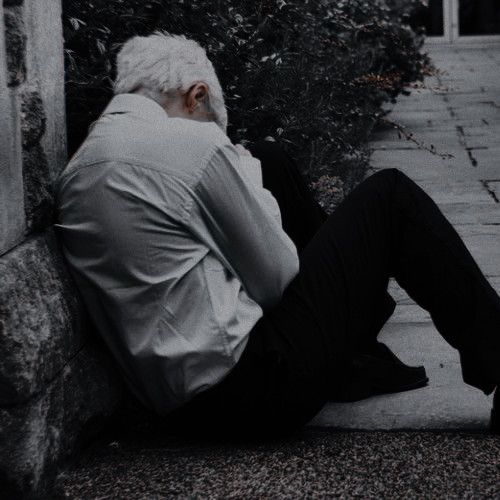 an old man sitting on the ground with his feet up against a wall and looking at something