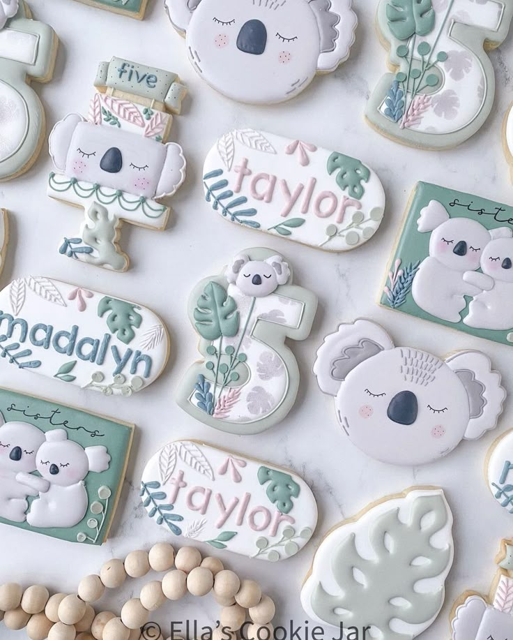 decorated cookies with koalas and eucalyptus leaves are displayed on a white tablecloth